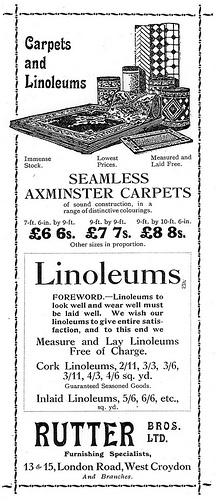 A tall, narrow black-and-white advert with a drawing of several carpets (rolled up and laid out flat) at the top. Text advertises “Carpets and Linoleums”, “Seamless Axminster Carpets”, and “we Measure and Lay Linoleums Free of Charge.” A decorative border is around the whole.