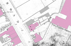 An extract from a map showing buildings and fields on either side of a road. Some of the buildings have been coloured pink and others have been coloured grey.