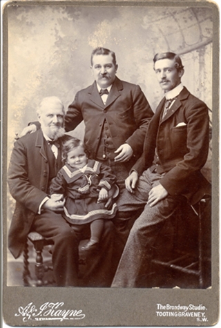 A sepia photo showing three white men and a white toddler, all with some facial resemblance. The oldest man is seated on the left; he has white hair and a white beard, and the toddler is on his lap wearing a sailor suit. The other men have short dark hair and moustaches.