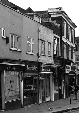 A black-and-white photo of terraced shops in varying architectural styles. The three shops on the left — Finlays, Clarks Bakery, and Leach Bros — are boxy and plain, while their neighbours to the right are more ornate.
