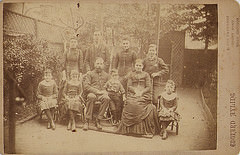 A sepia-toned photo showing a large family posing in the back garden of their home.  The parents are in their late 40s to early 50s, and the children range in age from about 4 to adult.