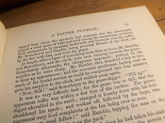 A page from Charles Dickens’ _Oliver Twist_, headed “A Pauper Funeral” and describing a hurried burial in a mass grave.