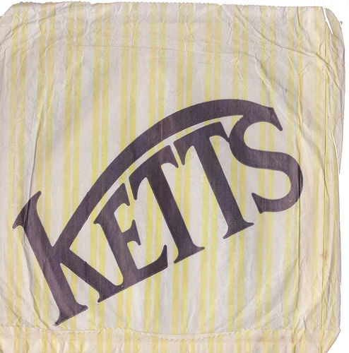 A square paper bag with yellow and white stripes and a large “Ketts” logo running diagonally upwards.