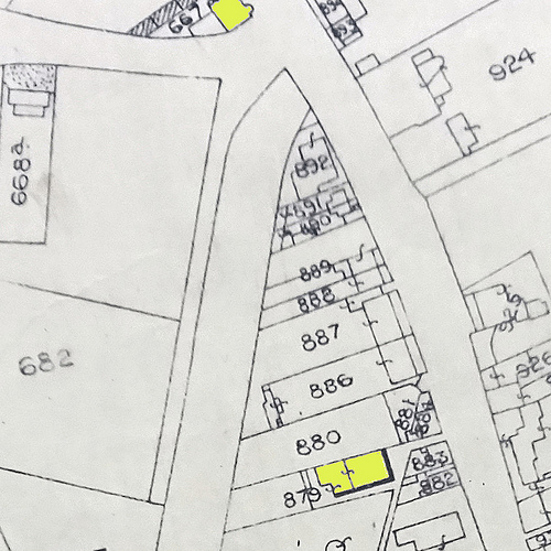 A map showing numbered plots; highlighted in yellow at the bottom is a building on plot 879.  What appears to be a narrow path leads slantwise from this between buildings to a wide road.