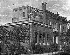 A black-and-white drawing or possibly photograph of a multi-level building with pillars at the entrance, surrounded by shrubs and trees.