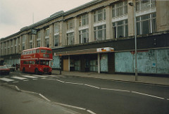 The same long three-storey building as above, but with the windows of the ground floor whitewashed over.  A Routemaster bus on route 109 is just passing over the zebra crossing at the front of the building.