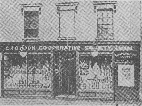 A black-and-white photo of a small terraced shopfront, with display windows on either side of a recessed central door and the name “Croydon Co‑operative Society Limited” above.