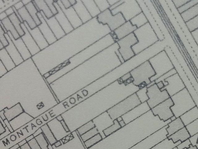A small section of a printed map.  A road with tramlines runs diagonally along the top right corner, and a side road off from this is labelled “Montague Road”.  Just to the north of Montague Road there are three houses adjoining each other, set back slightly from the main road.