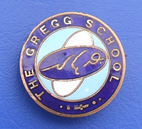 A similar badge but with no visible pin and what looks like a stylised aeroplace instead of the shield; the same shorthand symbols appear, but the wording this time reads “The Gregg School”.