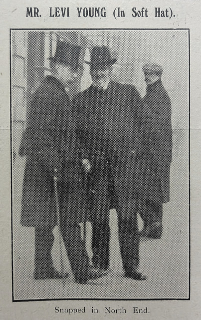 A black-and-white photo showing three men, one in a top hat, one in a soft-crowned hat, and one in a flat cap.  The man in the soft hat is smiling at the camera.  Text above reads “Mr. Levi Young (In Soft Hat).”, and text below reads “Snapped in North End.”