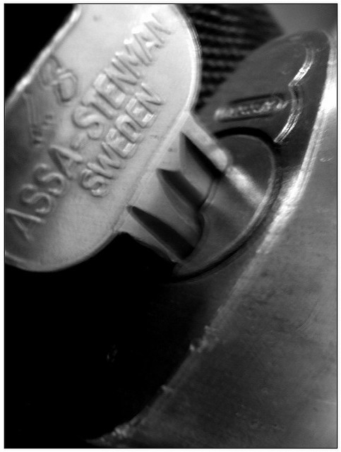 A blurry black-and-white close-up of a key in a lock. The words “Assa-Stenman Sweden” are embossed on the head of the key.