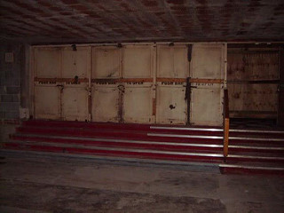 A wide set of four red-carpeted steps leading up to unpainted doors, below a low ceiling above an unfinished floor.