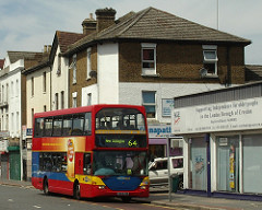 A double-decker red bus with the blind showing “New Addington 64”.  Behind the bus can be seen a corner shopfront with a sign reading “G[...]napat[...]”.