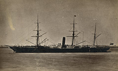 A sepia-toned monochrome photo of a ship at sea, with three tall masts and a smokestack.