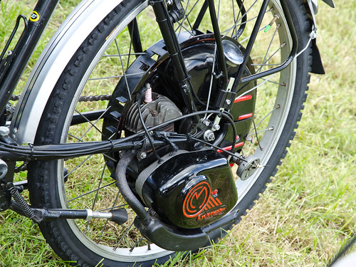 A close-up on a bicycle wheel with a black motor at the hub.  The bicycle is standing on grass.