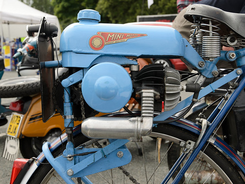 A small engine in a pale-blue casing, mounted on top of a bicycle wheel.  A couple of what look like motorised scooters are in the background.