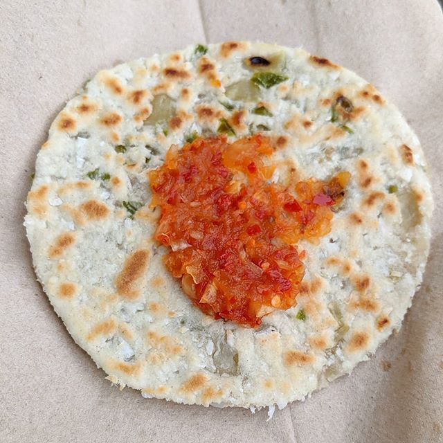 A small round onion-studded flatbread with a spoonful of red chilli chutney spread on top.