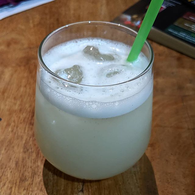 A glass tumbler containing a pale green liquid with ice cubes and froth on top.