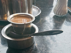 A metal cup of milky tea in a tall metal saucer.