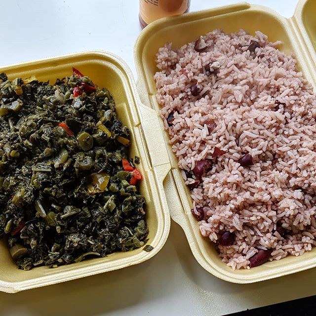 Styrofoam takeaway containers on a table.  One is filled with dark leafy greens cooked down with red chillies and onions, and the other with pink-tinged long-grain rice cooked with kidney beans.