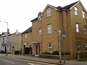 A fairly new-looking brick building with a gabled roof. Three storeys of windows are visible, though the top storey is in the gables. There's a garage port set into the left side of the ground floor. The Wandle Arms pub is visible to the left, with a few picnic benches outside.