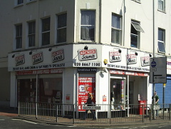 A corner shop with signs on the frontage reading “Richer Sounds / The UK’s Hi-Fi, Home Cinema & Flat Panel TV Specialists!”  Signs on the railings in front of the shop read “Oakfield Road” and “London Road”.