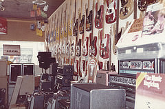 The interior of a small shop, with electric guitars hung on the wall and amplifiers piled up.