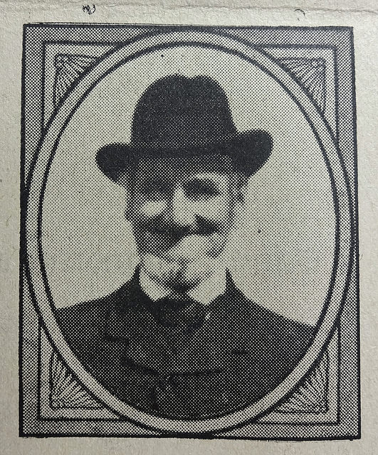 A black-and-white photo showing a smiling man with a white beard, wearing a soft-crowned hat and a dark suit.