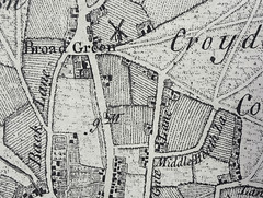 Map showing roads, enclosed areas with buildings, and large expanses either lined as if to indicate cultivated fields or with small marks resembling tufts of grass.