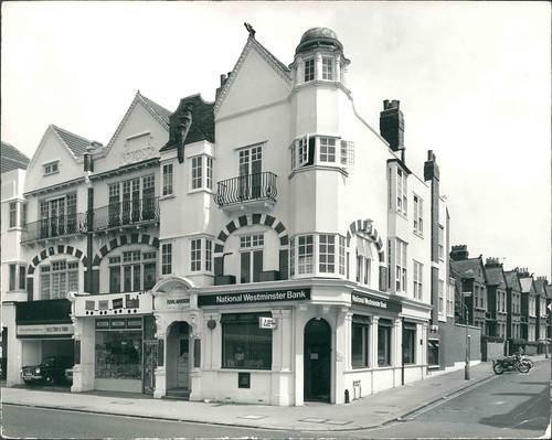 A similar view to the previous image.  The brickwork here seems to have been rendered over and painted white, obscuring some of the details that were visible earlier.  The dome is still present.  The sign on the corner property now reads “National Westminster Bank”.