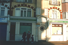 A view of the same corner property, taken straight on from the London Road side.  A very simple sign reads “Viet Hoa Restaurant / Authentic Vietnamese Cuisine”.  An adult and a child are standing on the pavement in front, looking at the camera, while two other adults walk past behind them.