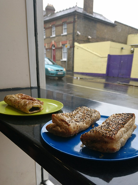Two plastic plates with large sausage rolls on, two of them topped with poppy seeds.